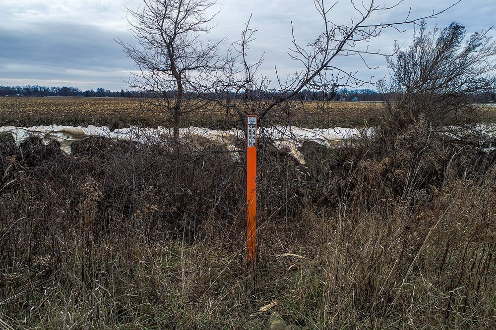 An orange fiberglass witness post standing near a section corner in a field